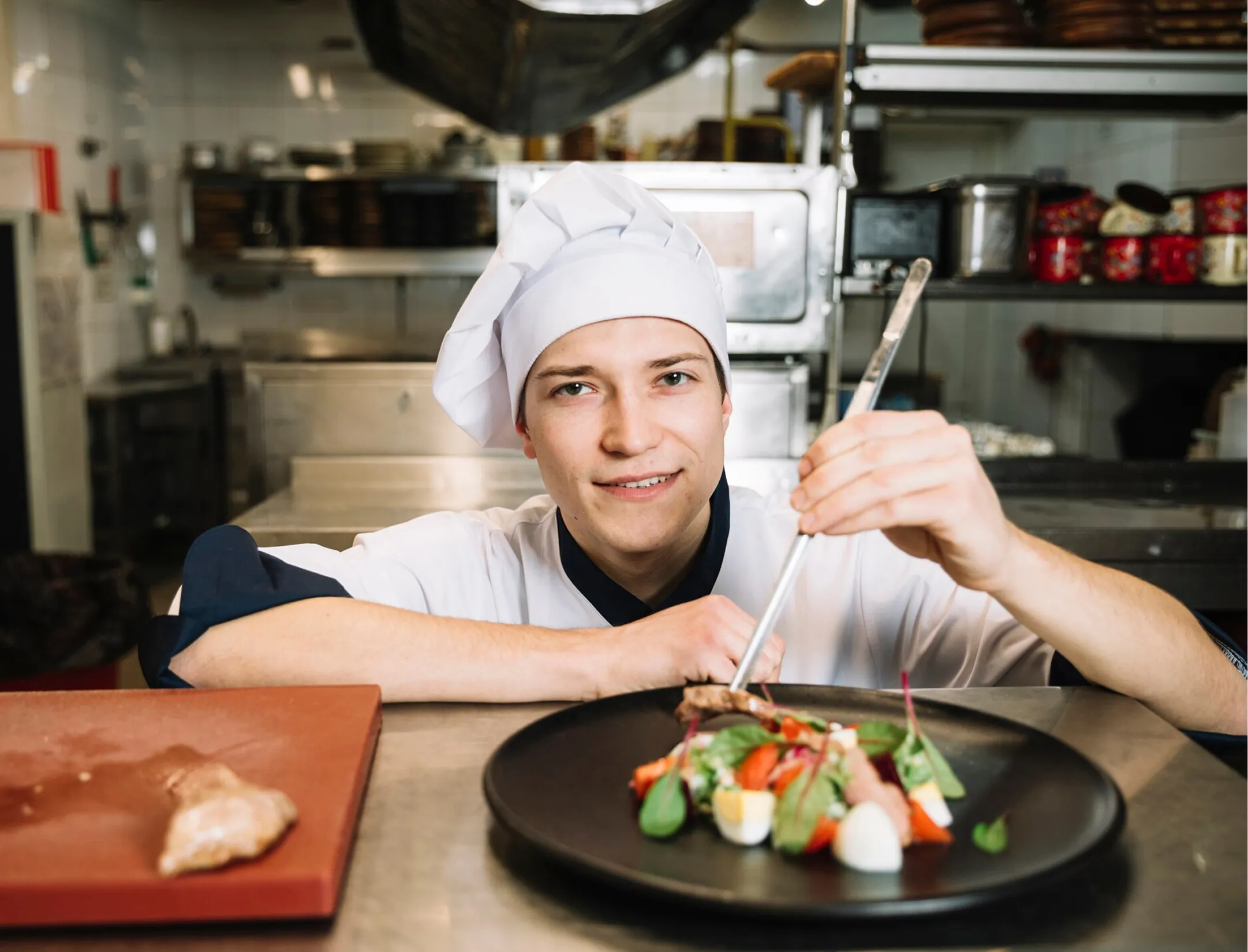 Chef wearing a chef hat, holding a fork in one hand and a knife in the other, ready to prepare a meal.