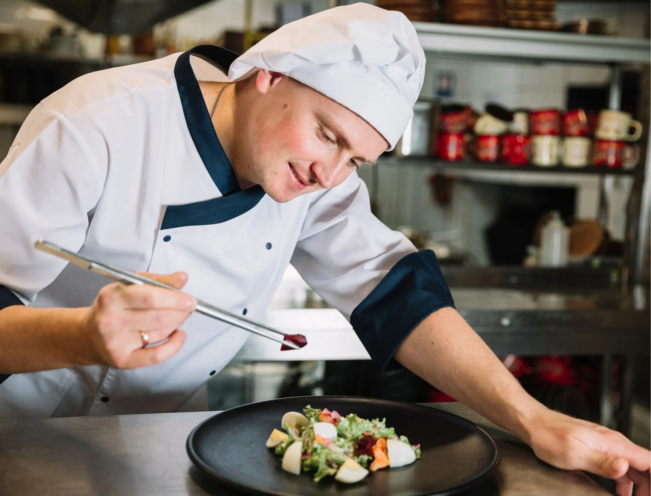 A chef in a white hat is focused on preparing ingredients in a professional kitchen.